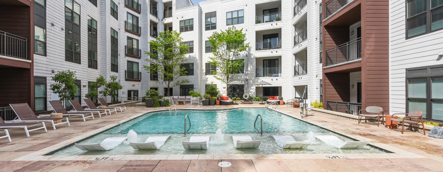 a swimming pool in a courtyard between buildings with lounge chairs